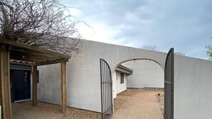 Un espace extérieur abrité, doté d’un mur en béton, d’une pergola en bois et d’un portail en métal.