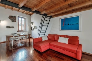 Una habitación con techo de madera, un sofá rojo, una mesa de comedor con sillas, una escalera y un cuadro azul en la pared.