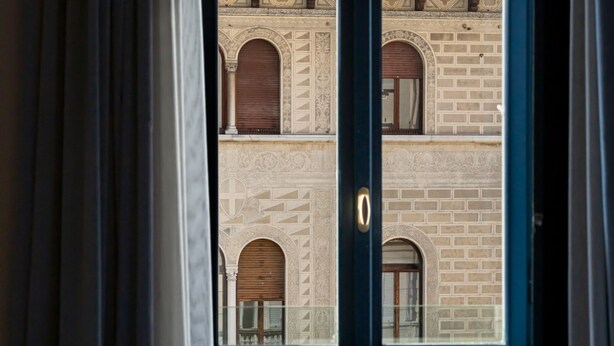 A view through a window with a door, revealing a building with arched windows and patterned brickwork. - Sky Suite - My Home in Como (Como)