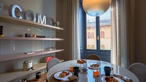 A dining area with a table set for breakfast, a window with a view of buildings, and shelves with decorative items. - Sky Suite - My Home in Como (Como)