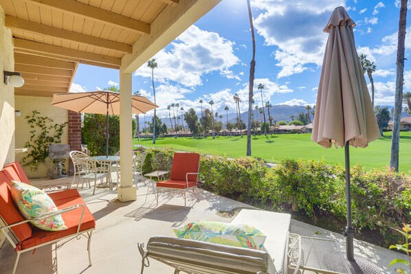 A covered outdoor patio with lounge chairs, a table, and umbrellas. - Palm Desert Condo w/ Patio & Golf Course Views (Palm Desert)