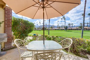 A patio with a table and chairs under a large umbrella, overlooking a golf course with palm trees and a mountain in the distance. - Palm Desert Condo w/ Patio & Golf Course Views (Palm Desert)