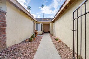 A narrow pathway leading to a building with a door and windows, surrounded by cacti and a palm tree. - Palm Desert Condo w/ Patio & Golf Course Views (Palm Desert)