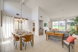 A spacious living area with a dining table, chairs, a sofa, and a large window offering a view of the outdoors. - Palm Desert Condo w/ Patio & Golf Course Views (Palm Desert)