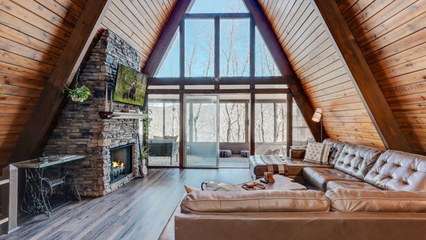 Une pièce chaleureuse de style loft, dotée d’une cheminée en pierre, d’un canapé en cuir et de grandes fenêtres offrant une vue sur les arbres.