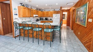 A kitchen with wooden cabinets, a central island with chairs, and a refrigerator. - Oceanside, Hot Tub, Rec Room, OD1, The Sandy Dune (Duck)