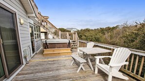 A wooden deck with a table and two Adirondack chairs, a set of stairs leading to a covered area, and a view of a house in the background. - Oceanside, Hot Tub, Rec Room, OD1, The Sandy Dune (Duck)