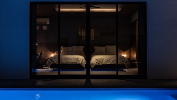 A modern bedroom with two beds, a ceiling fan, and a pool in the foreground. - CLASS THE FIRST (Miyakojima)