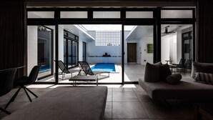 A modern living room with a large sliding glass door leading to a pool area. - CLASS THE FIRST (Miyakojima)