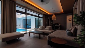 A modern living room with a sofa, a bench, and a coffee table. There is a large window with curtains, a ceiling fan, and a hanging light fixture. - CLASS THE FIRST (Miyakojima)