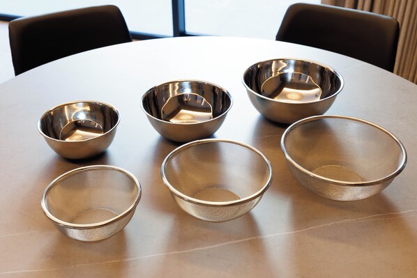 Une table ronde avec cinq bols métalliques et une passoire.