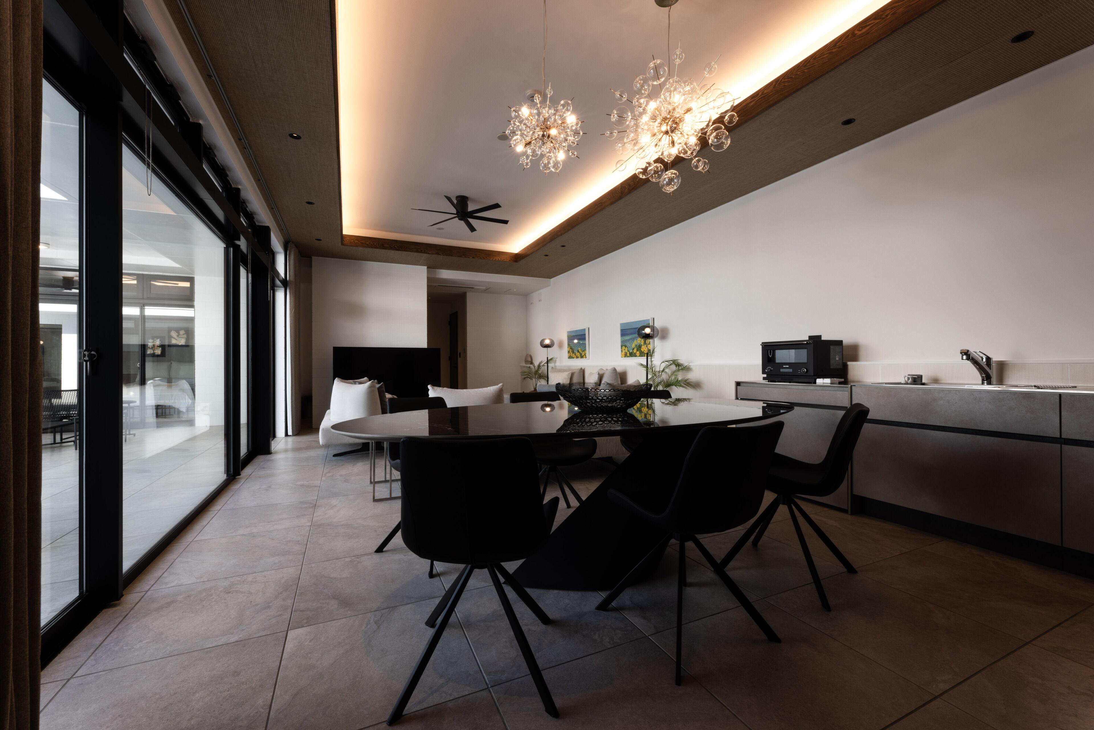 A modern kitchen with a dining area, featuring a large island, black chairs, and a chandelier.