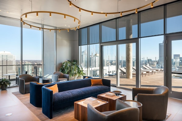 Un salón moderno con un sofá azul, sillones de cuero y un amplio ventanal con vistas a la ciudad.