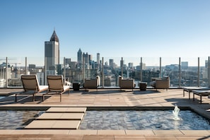 Un área de piscina en la azotea con sillones de descanso y una fuente, con vistas a un horizonte urbano.