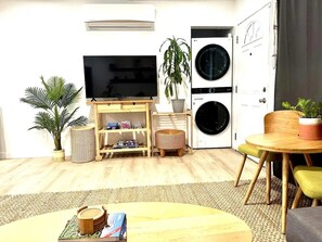 A living room with a TV, a washing machine, a dining table, and a small stool.