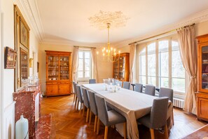 A dining room with a long table, chairs, a chandelier, and wooden cabinets.