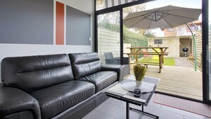 A modern living room with a black leather sofa, a glass door leading to an outdoor patio with a table and umbrella. - Maison Labennaise - Welkeys (Labenne)