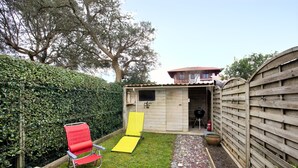 A backyard with a wooden fence, a red chair, a yellow slide, and a barbecue area. - Maison Labennaise - Welkeys (Labenne)