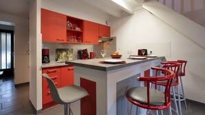 A modern kitchen with red cabinets, a central island with bar stools, and a staircase leading to an upper level. - Maison Labennaise - Welkeys (Labenne)