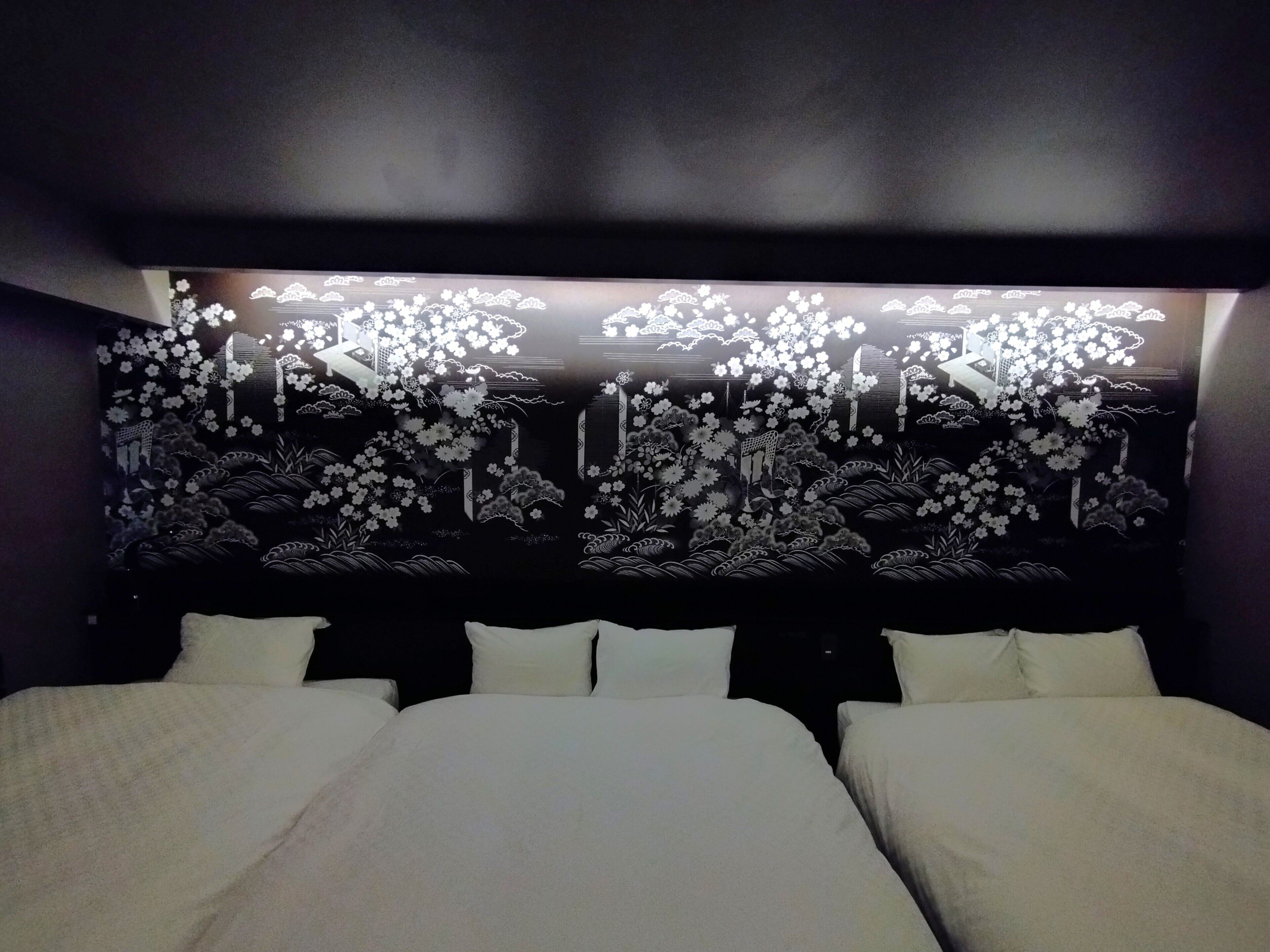Quarto de hotel com uma cama grande, cabeceira com design floral e uma parede escura.