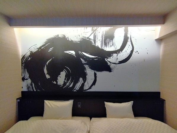 Habitación de hotel con un cuadro abstracto grande en la pared, cabecero oscuro y dos almohadas blancas.