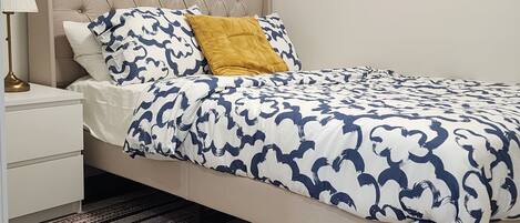 A bedroom with a bed, nightstand, lamp, and a framed picture on the wall.