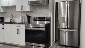 A modern kitchen with white cabinets, stainless steel appliances, and a wood-patterned floor. - Family Friendly 2-Bedroom Oasis Awaits! (Calgary)