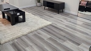 A modern living room with a flat-screen TV mounted on the wall, a black entertainment unit, a coffee table, and a potted plant. - Family Friendly 2-Bedroom Oasis Awaits! (Calgary)