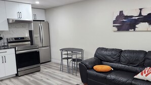 A modern living space with a kitchen, a black leather sofa, a small round table, and a coffee table. - Family Friendly 2-Bedroom Oasis Awaits! (Calgary)