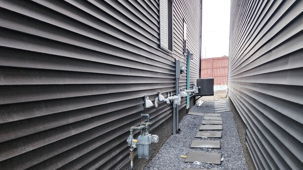A narrow alleyway with corrugated siding walls, a utility box, and a ventilation unit. - Family Friendly 2-Bedroom Oasis Awaits! (Calgary)