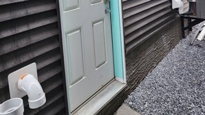 A house with a grey door, a small window, and a grey exterior wall. - Family Friendly 2-Bedroom Oasis Awaits! (Calgary)