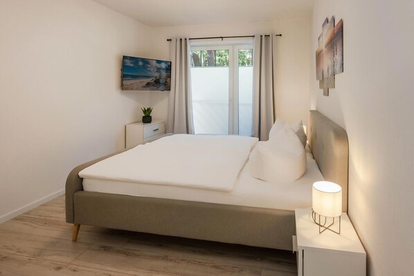A bedroom with a bed, bedside table, lamp, and a window with curtains.