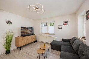 Un salon moderne avec un téléviseur à écran plat, un canapé gris, un meuble en bois et une petite table sur laquelle est posée une plante.