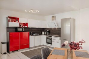 Une cuisine moderne avec des meubles blancs, un réfrigérateur rouge et un four encastré.