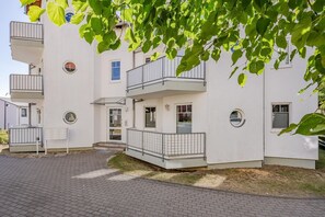 A multi-story residential building with balconies, a small entrance, and a paved driveway.