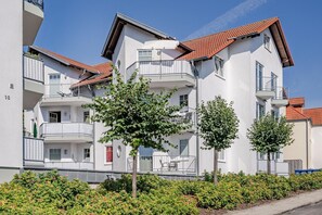 A multi-story residential building with balconies, a clear sky, and well-maintained greenery.