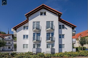 A multi-story residential building with balconies, a pitched roof, and a clear sky.