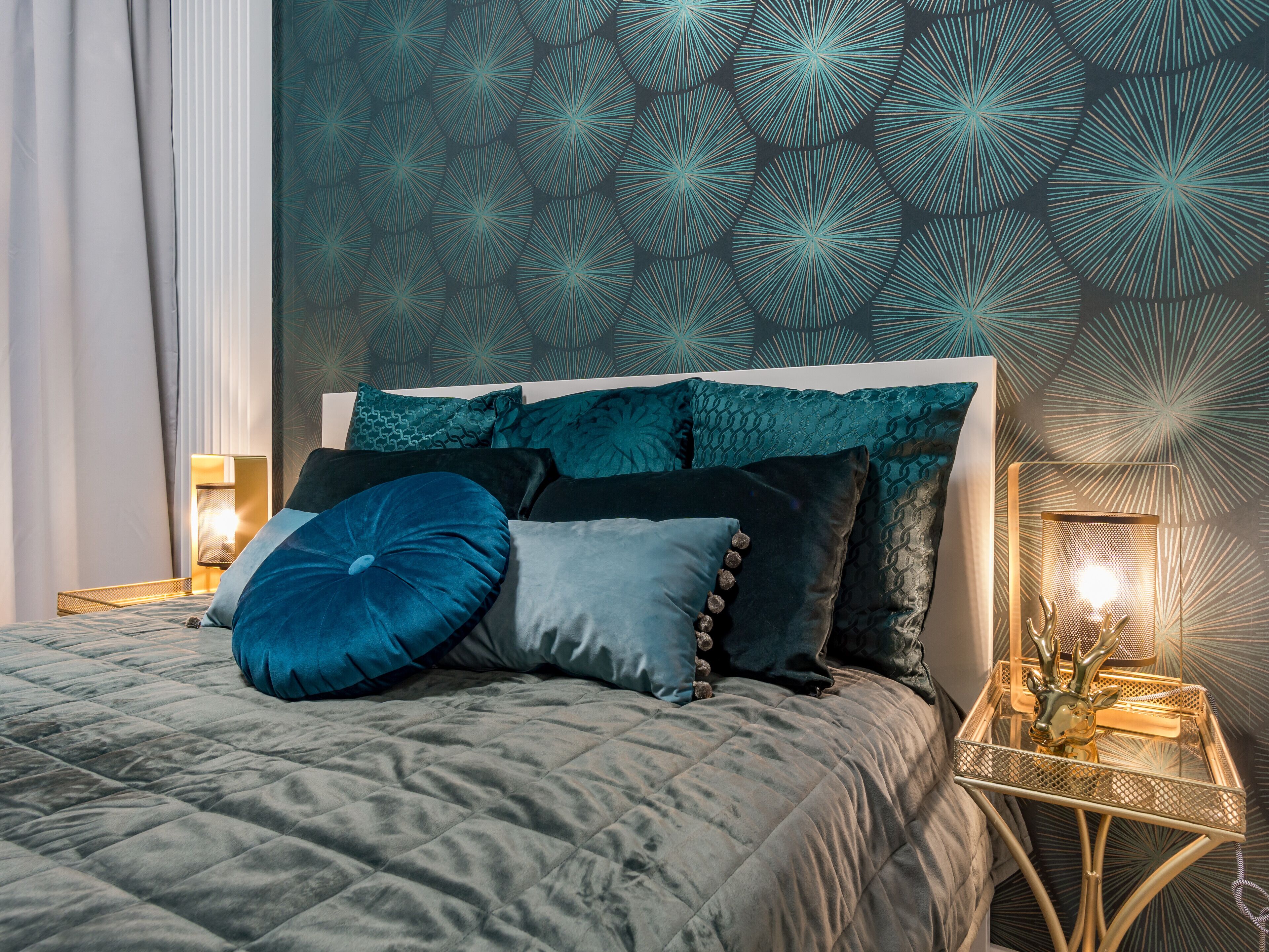 Ein ordentlich bezogenes Bett mit einer gesteppten, grauen Bettdecke, mehreren Kissen in Blau- und Grautönen und einem dekorativen Kopfteil.