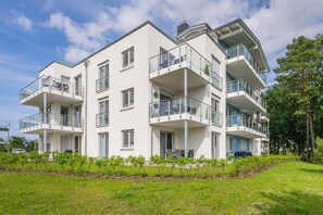 Un immeuble résidentiel à plusieurs étages, doté de balcons, d’un toit plat et d’un espace verdoyant à l’avant.