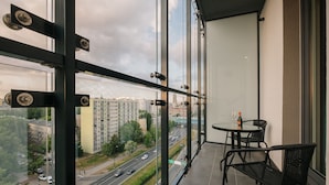 Ein Balkon mit Glastrennwand, einem runden Tisch und Stühlen sowie einer Weinflasche.
