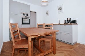 A modern kitchen with a wooden dining table and chairs, a built-in oven, and a coffee maker on the countertop. - Ferienwohnung Ole - Traumhafte Ferienwohnung mit Platz zum Arbeiten, Wlan und Terrasse (Heringsdorf)