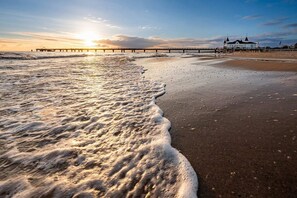 Una playa con olas, un muelle y un edificio de techo puntiagudo.