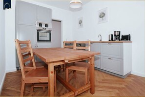A compact kitchen with white cabinets, a wooden dining table, and a coffee maker.