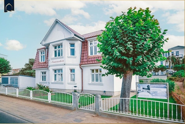 A two-story house with a red roof and white walls, labeled "Haus Sonnenschein."