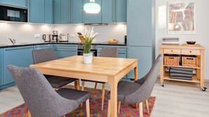A modern kitchen with teal cabinets, a wooden dining table, and grey chairs. - Ferienwohnung Haffblick 1 - Ferienapartment in Ruhiger Lage für 2 Personen, mit Terrasse (Zirchow)