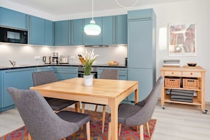 A modern kitchen with teal cabinets, a wooden dining table, and grey chairs.