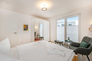 Une chambre d’hôtel avec un lit, une chaise, une petite table, un tableau et une vue sur l’extérieur.