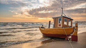 A wooden boat with a cabin, moored on a sandy beach with waves. - Ferienwohnung Haffblick 1 - Ferienapartment in Ruhiger Lage für 2 Personen, mit Terrasse (Zirchow)
