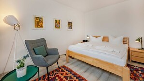 A bedroom with a bed, a chair, a bedside table, a lamp, and wall art. - Ferienwohnung Haffblick 1 - Ferienapartment in Ruhiger Lage für 2 Personen, mit Terrasse (Zirchow)