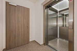 A hallway with a wooden door and a modern elevator.